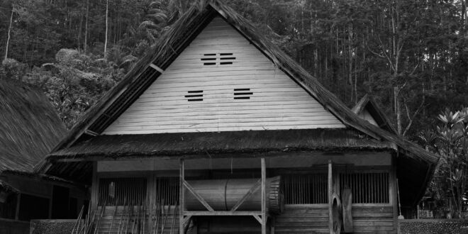 Rumah semi permanen sederhana dengan atap genteng, dinding kayu, dan taman kecil, cocok untuk keluarga muda.