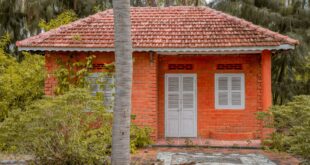 Model rumah sederhana dengan atap genteng, dinding bata, dan taman kecil di depan
