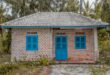 Rumah sederhana kampung dengan atap ijuk, dinding kayu, dan halaman penuh tanaman tropis.