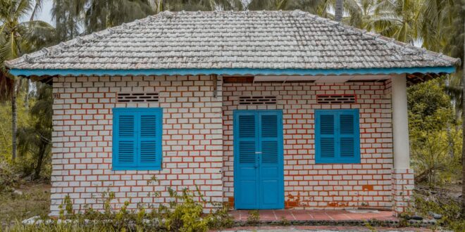 Gambar rumah sederhana berukuran 5x7 meter dengan desain minimalis, atap merah, dan taman kecil di depannya.