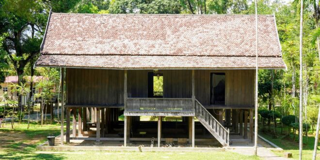 Contoh rumah panggung sederhana dengan atap jerami, tiang kayu, dan teras terbuka di lingkungan tropis