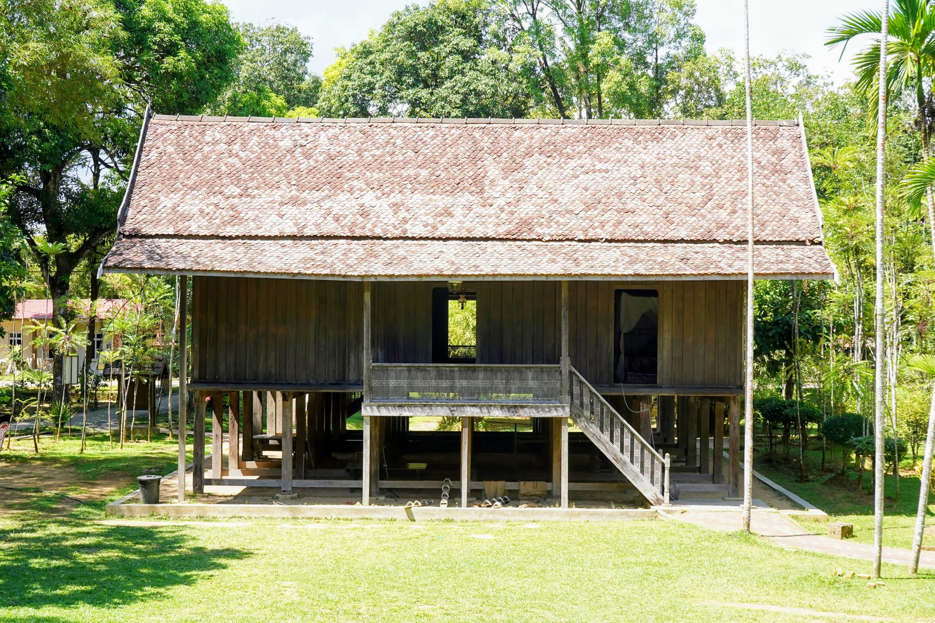 Contoh rumah panggung sederhana dengan atap jerami, tiang kayu, dan teras terbuka di lingkungan tropis