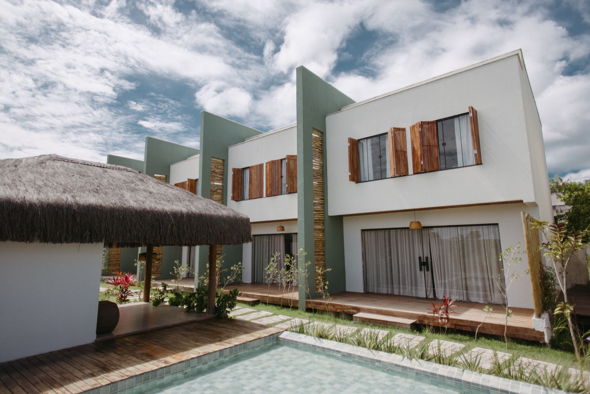 Desain villa sederhana dengan tampilan modern, atap rendah, dan taman hijau mengelilingi rumah.