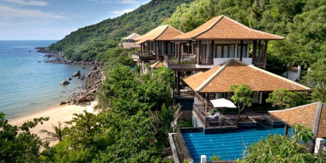 Desain villa sederhana dengan fasad modern, atap datar, dan taman hijau yang menambah kesan alami.