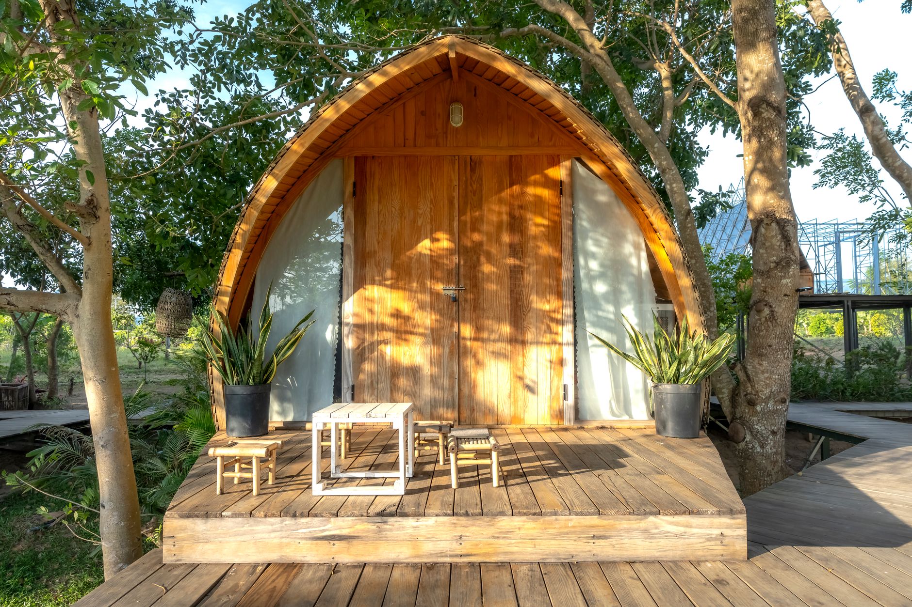 Rumah kayu kecil sederhana dengan atap miring, dikelilingi pepohonan hijau, tampak nyaman dan alami.