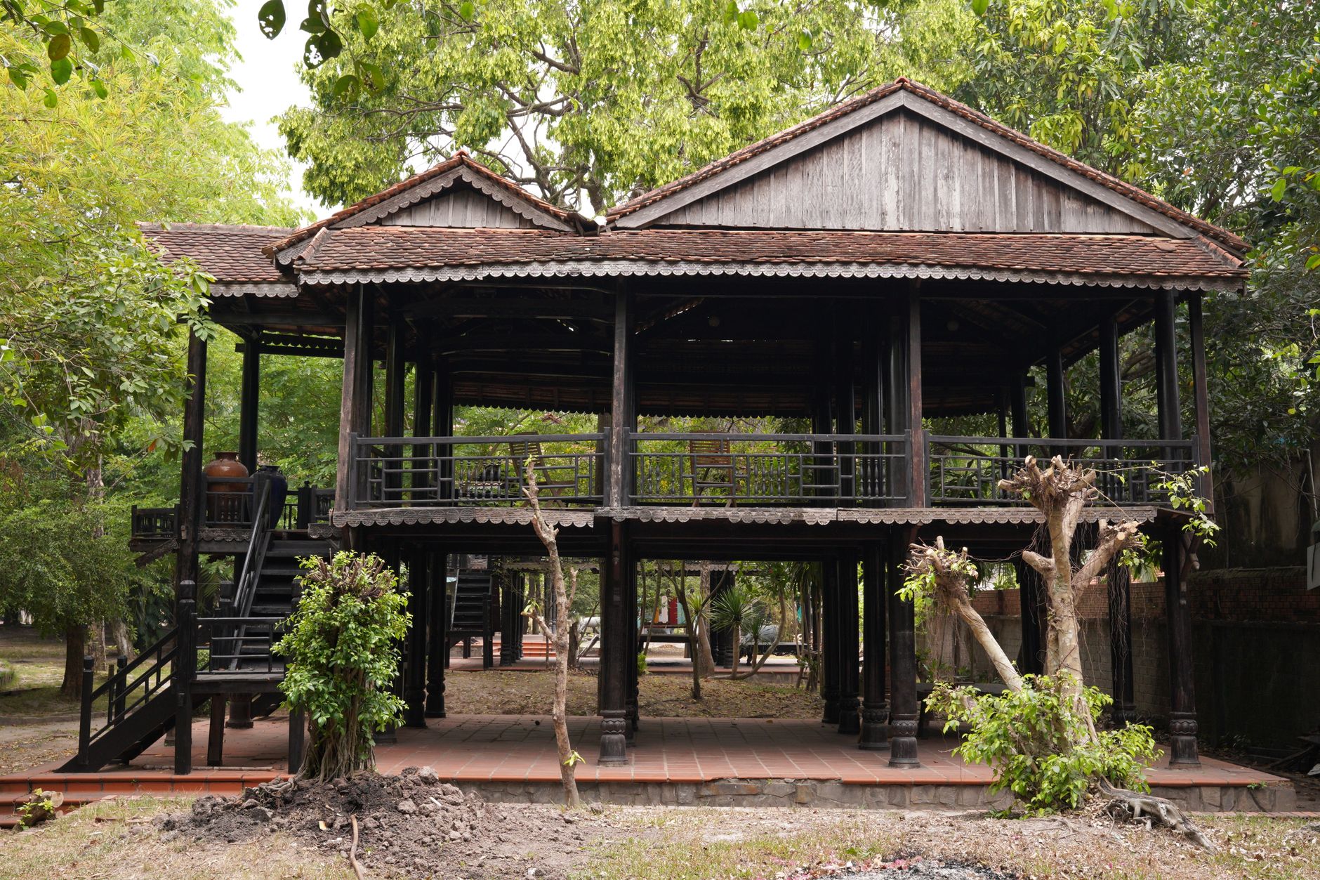 Rumah panggung sederhana dengan atap jerami, dinding kayu, dan teras terbuka di lingkungan tropis.
