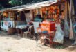 Desain warung sembako sederhana dengan rak kayu, pencahayaan alami, dan nuansa warna cerah di kampung.