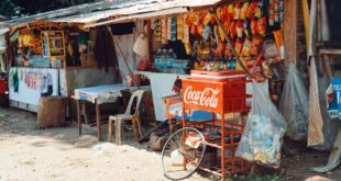 Desain warung sembako sederhana dengan rak kayu, pencahayaan alami, dan nuansa warna cerah di kampung.