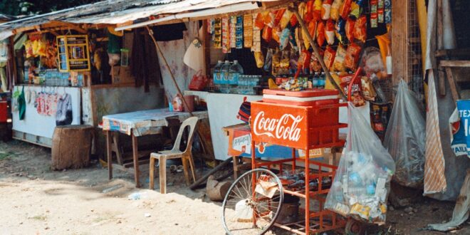 Desain warung sembako sederhana dengan rak kayu, pencahayaan alami, dan nuansa warna cerah di kampung.