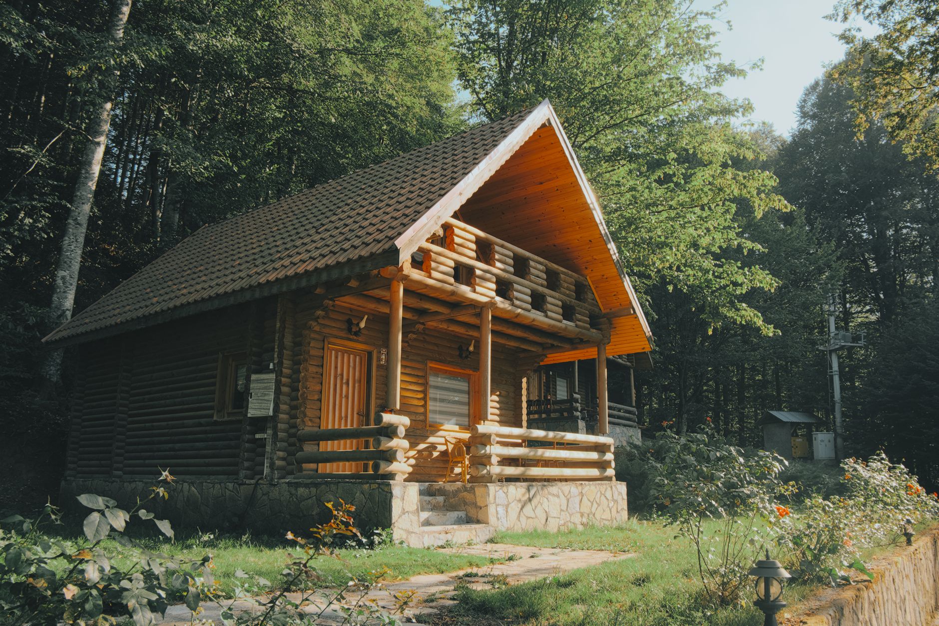 Rumah kayu kecil sederhana dengan atap miring, jendela putih, dan taman hijau di latar belakang.